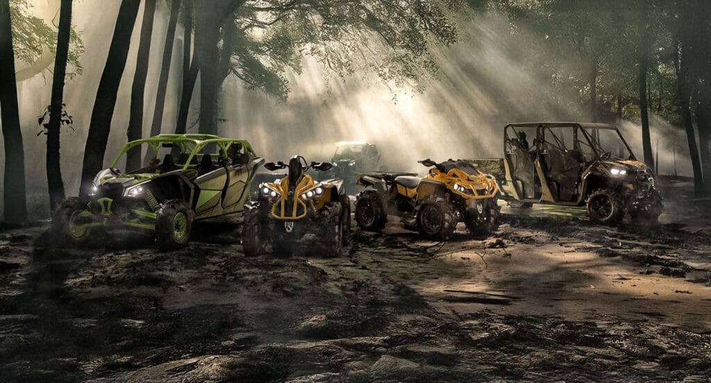 Multiple off-road ATVs, UTVs, and side-by-sides arranged in a line in a lush Ontario forest.