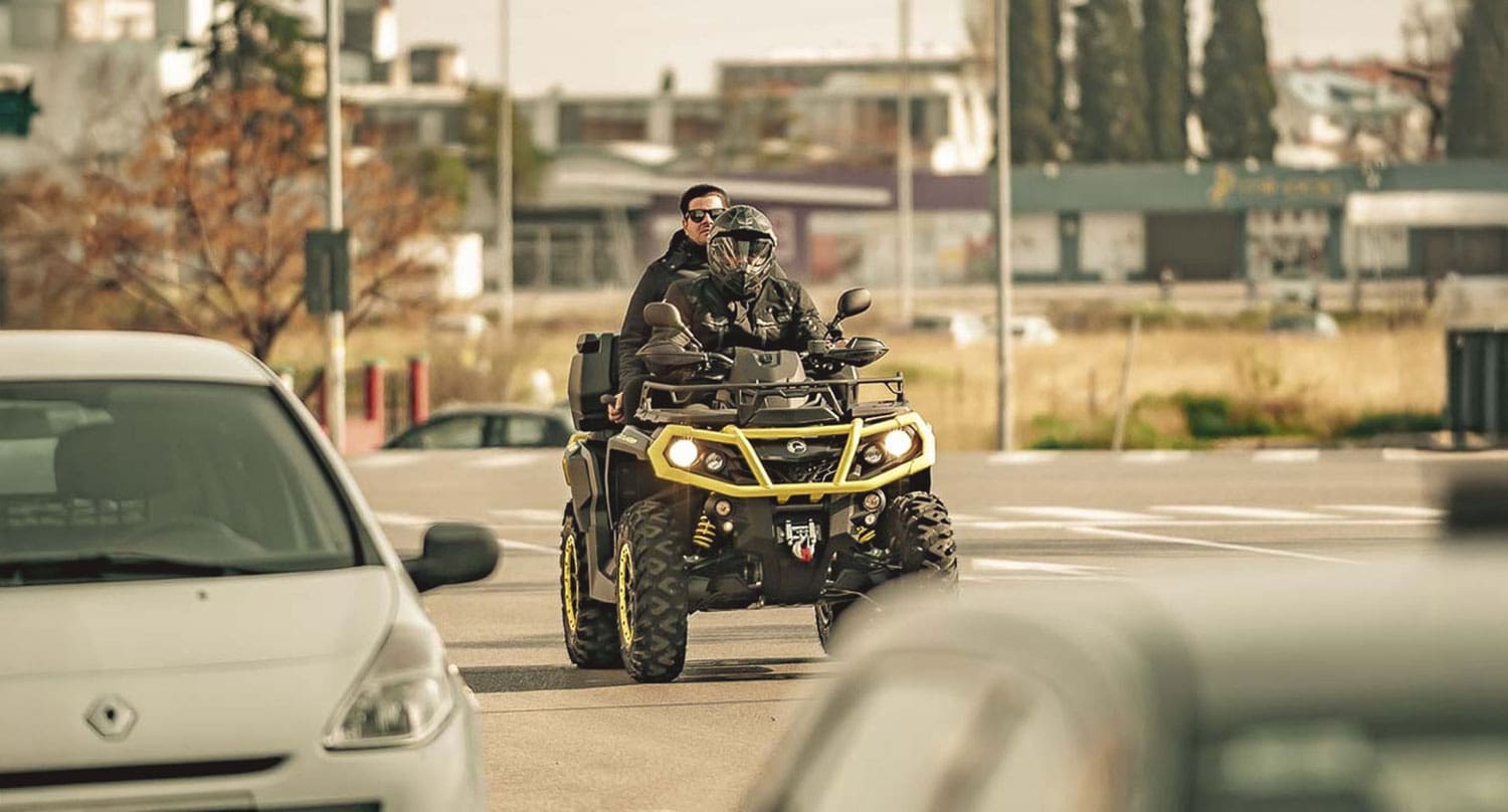 Two people wearing helmets riding a quad bike on a paved road, showcasing off-road vehicle versatility in Ontario.